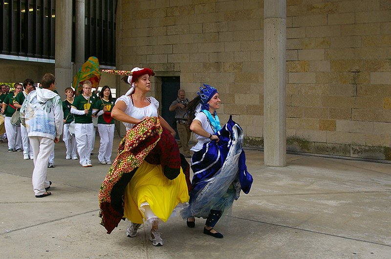 2 women in bright dresses lead a parade