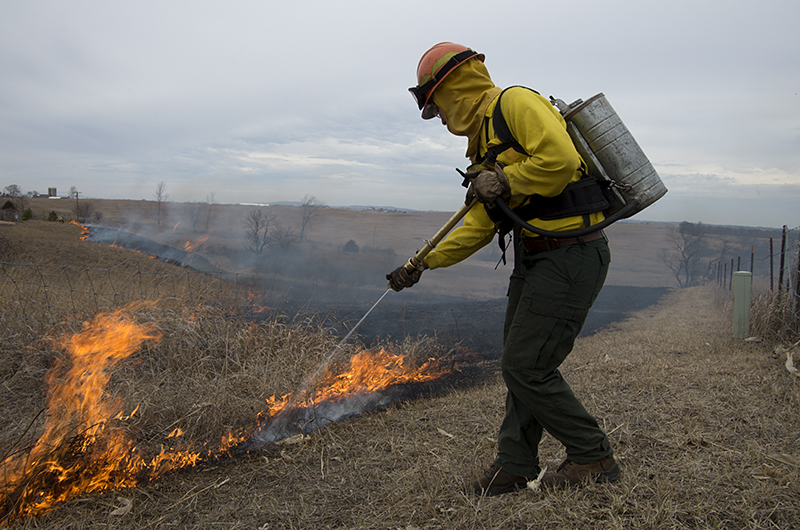Woman spraying the edge of a controlled burn with a water pack